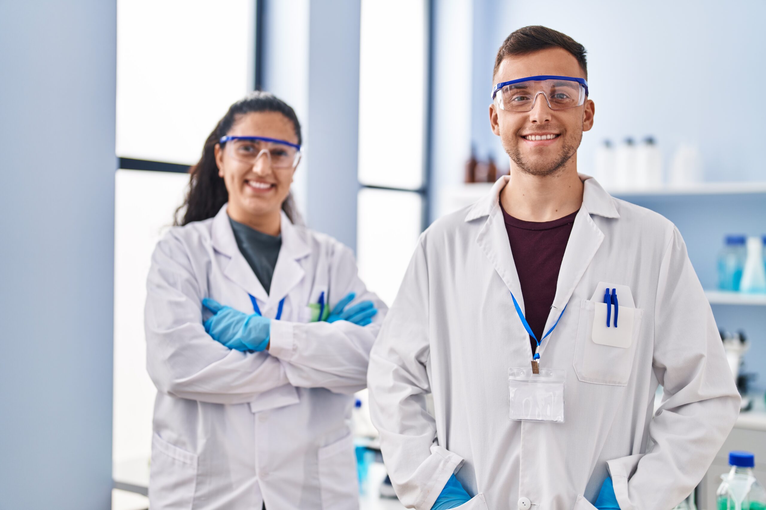 Man and woman wearing scientist uniform standing with arms crossed gesture at laboratory